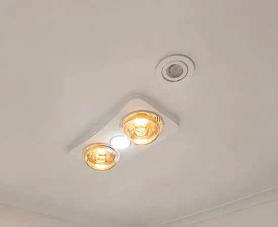 Two-lamp 3-in-1 heat, light and exhaust unit fitted to a white bathroom ceiling beside an LED downlight