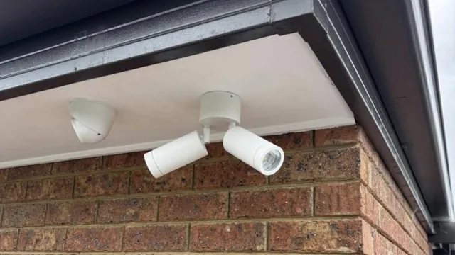 Turret camera beside twin spotlights under the eave of a brick home
