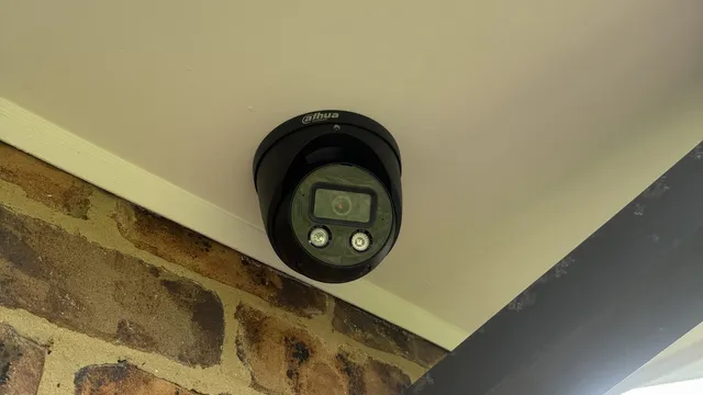 Black turret camera under a cream eave beside a dark grey beam