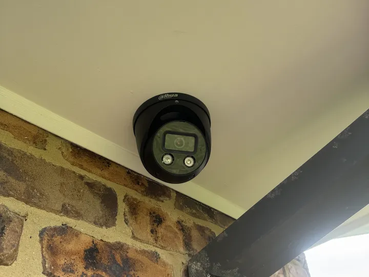 Black turret camera under a cream eave next to a dark grey beam