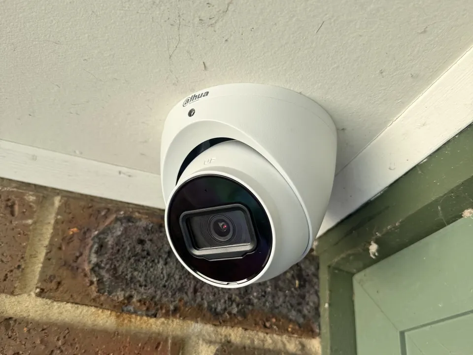 White turret camera at the corner of a painted eave above a window