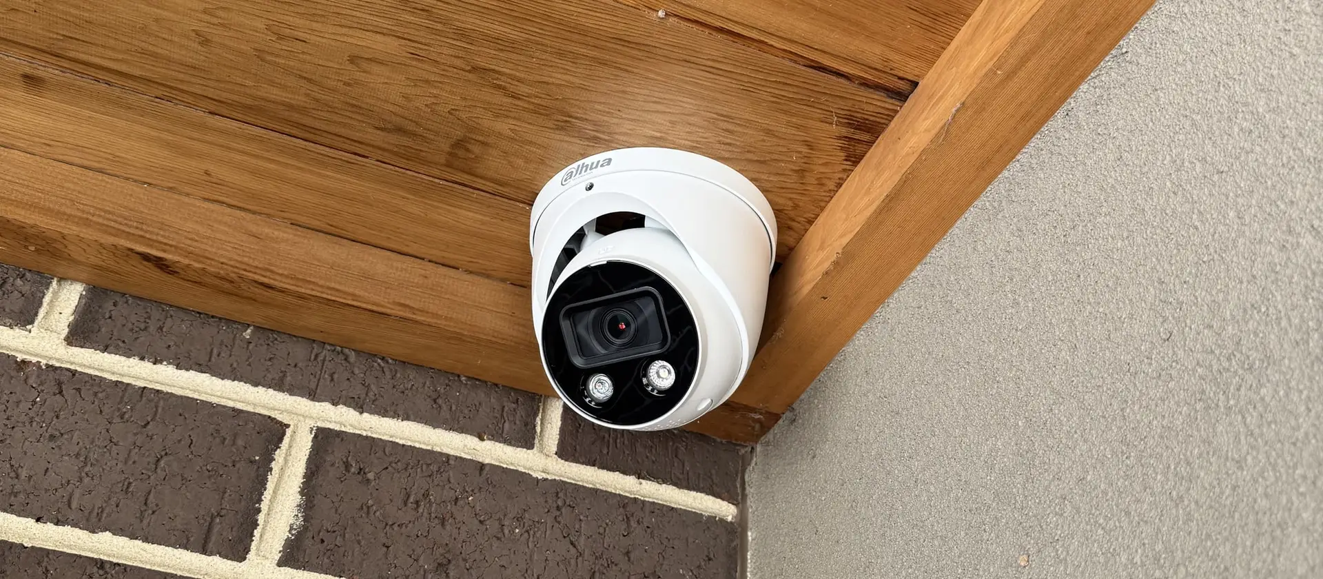 Hard-wired turret security camera fitted under the timber-lined eave of a brick home