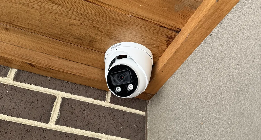 Hard-wired turret security camera fitted under the timber-lined eave of a brick home