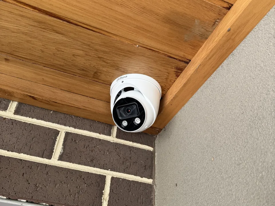 White turret camera fitted under the timber-lined eave of a brick home