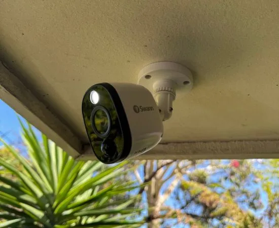 Outdoor security camera with floodlight mounted under the eave of a building