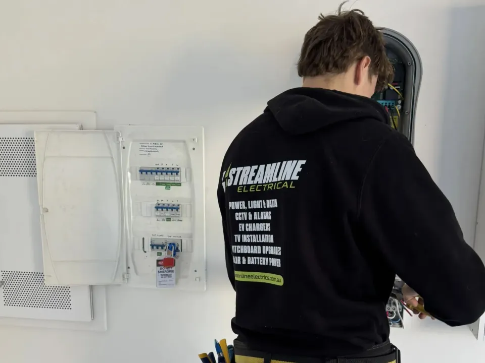 Streamline electrician working at an open switchboard with a do-not-energise tag on the main switch