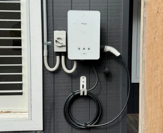 Wall-mounted home EV charger with its cable installed on a dark weatherboard exterior