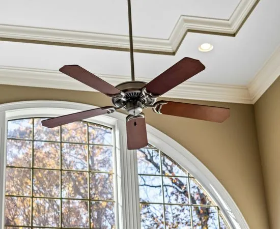 Ceiling fan installed on an ornate ceiling beside an arched window