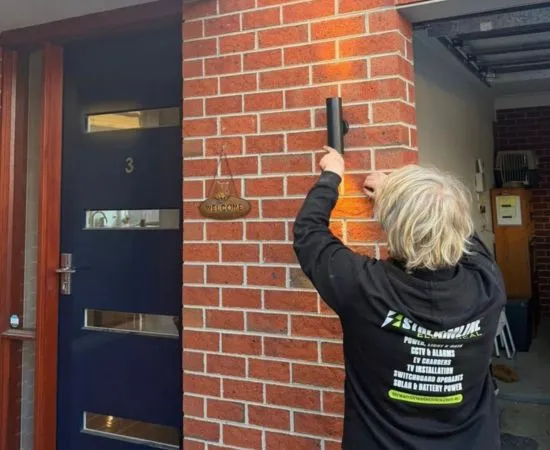 Streamline electrician fitting an outdoor wall light beside the front door of a brick home