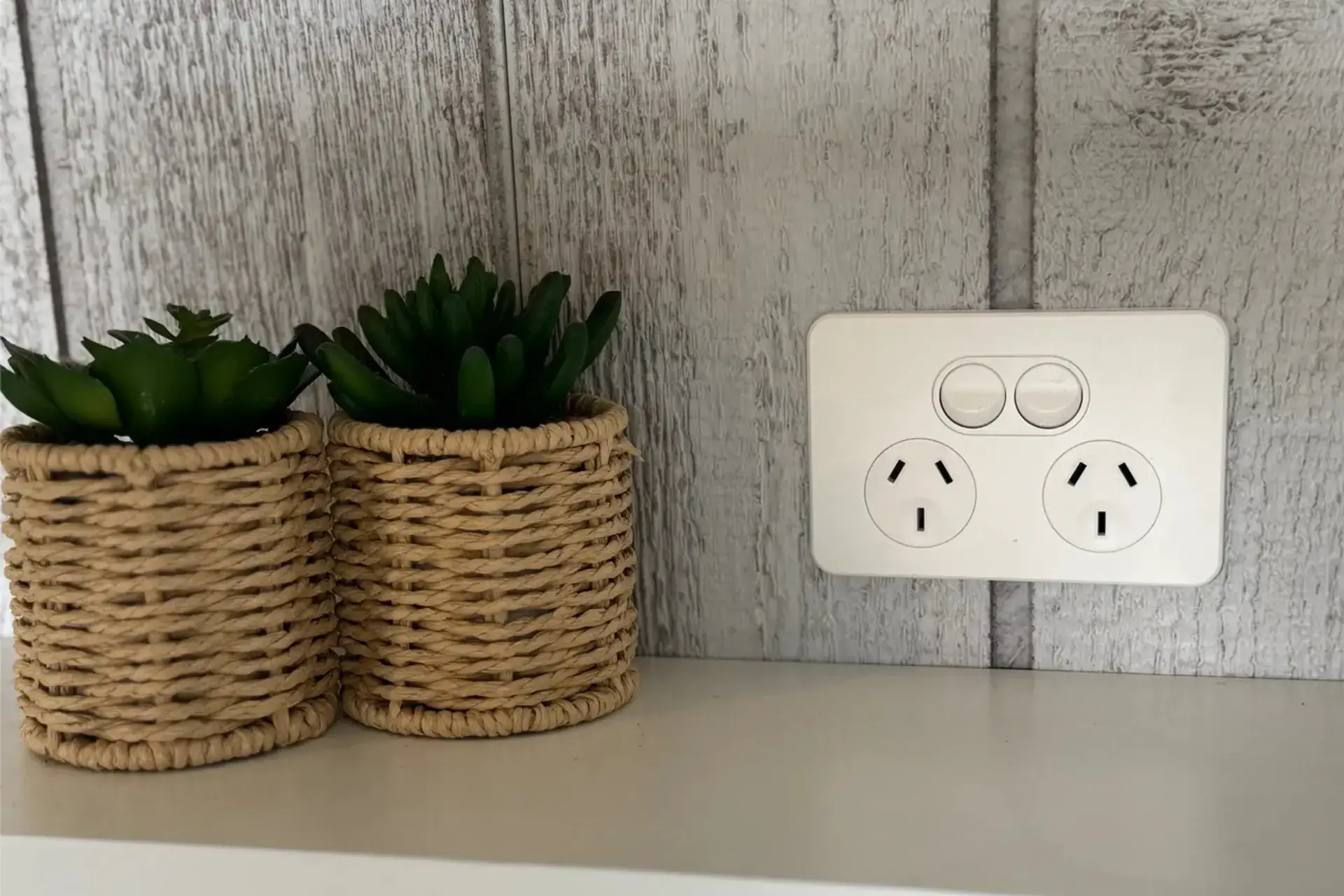 New double power point on a white timber-panel wall beside two woven planters