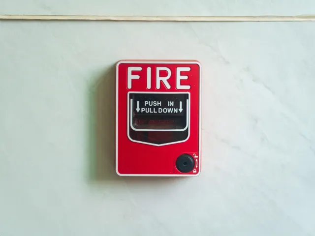 Red manual fire alarm pull station mounted on a marble wall