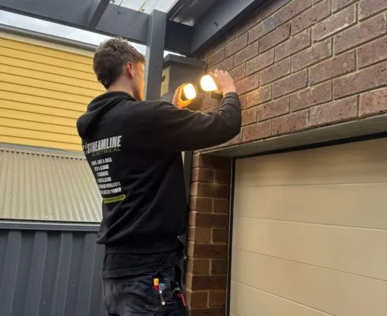 Electrician installing a twin-head sensor security light above a garage door in Frankston