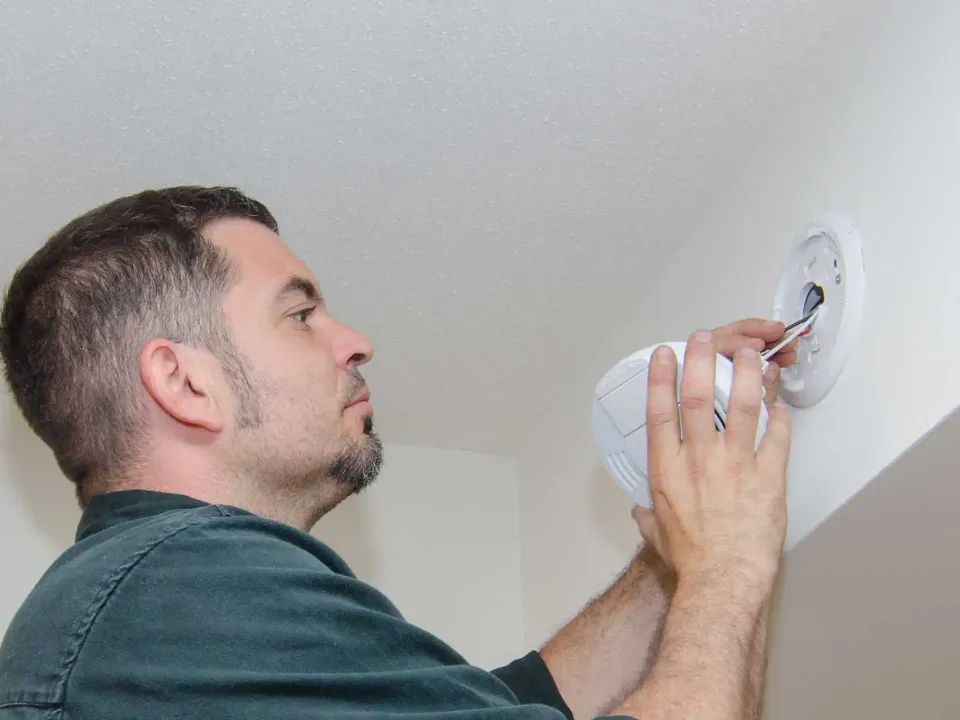 Electrician replacing a battery smoke alarm with a hard-wired unit