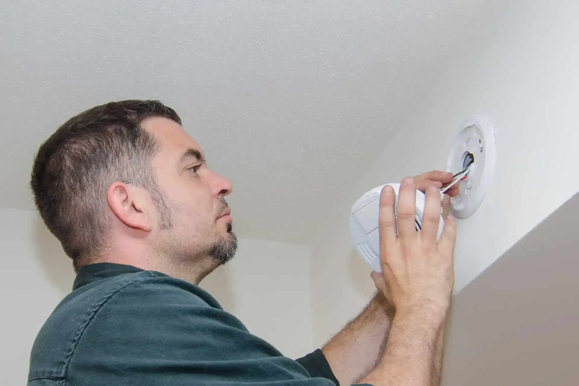 Electrician fitting a hard-wired smoke alarm to a ceiling