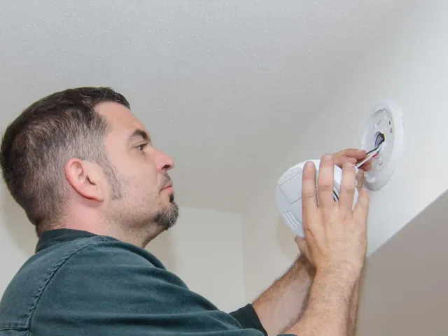 Electrician fitting a hardwired smoke alarm to a ceiling
