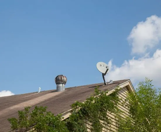 Satellite dish and whirlybird roof vent on a house roof against a blue sky
