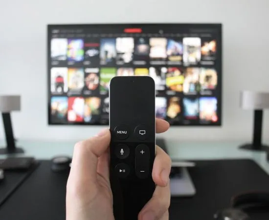 Hand holding a remote in front of a smart TV showing streaming apps